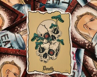 May include: A sticker with a vintage design featuring a skull with mushrooms growing out of its eye sockets. The sticker has a tan background with a red border and the word "Death" in a gothic font.