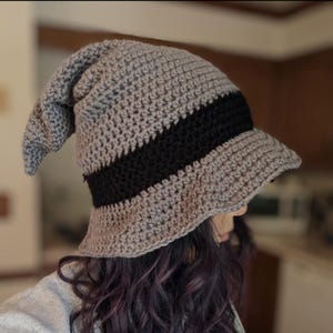 May include: Gray and black crocheted hat with a pointed top and a wide brim. The hat is worn by a person with long, dark hair.