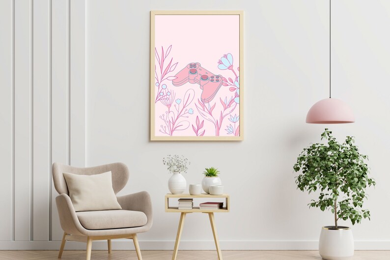 May include: A framed art print featuring a pink video game controller design surrounded by pink and blue floral elements. The artwork is set against a light pink background, creating a soft, feminine aesthetic. The frame is a light wood color.