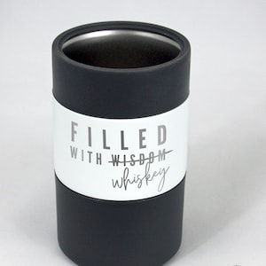 May include: A black and silver insulated tumbler with the words "FILLED WITH WISDOM whiskey" printed on a white band. The tumbler has a matte black base and a silver interior.