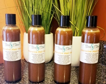 May include: Four brown bottles of "Intensive Hair Mask" with black caps and white labels. The labels include the brand name "Sissi's Eden" and a list of ingredients. The bottles are arranged in front of green plants.