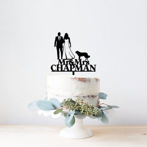 May include: Black silhouette cake topper featuring a bride and groom holding hands with a dog. The topper says "Mr. & Mrs. Chapman" in black lettering.