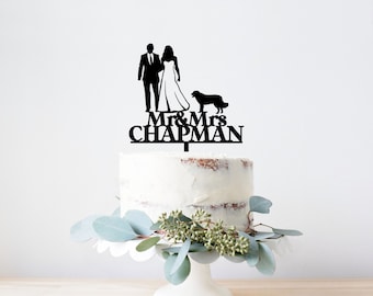 May include: Black silhouette cake topper featuring a bride and groom holding hands with a dog. The topper says "Mr. & Mrs. Chapman" in black lettering.