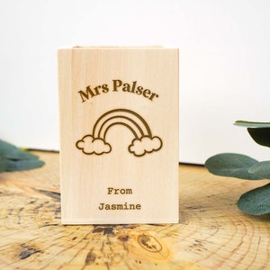 May include: A wooden box with a rainbow and clouds design. The box is engraved with the text "Mrs. Palser" and "From Jasmine".