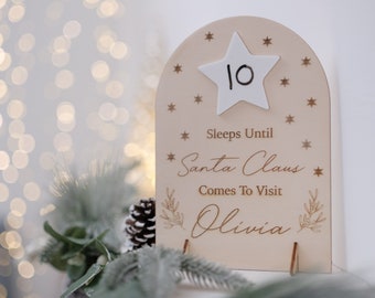 Könnte beinhalten: Ein hölzernes Countdown-Schild mit einem weißen Stern, auf dem "10" steht. Das Schild sagt "Schläft bis zum Besuch des Weihnachtsmanns bei Olivia".