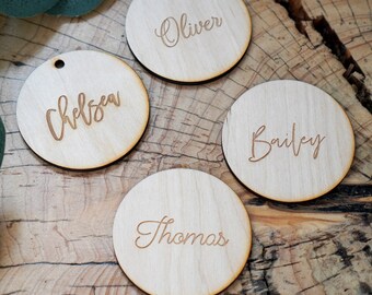 May include: Four round wooden tags with names written in cursive. The names are Chelsea, Oliver, Bailey, and Thomas.