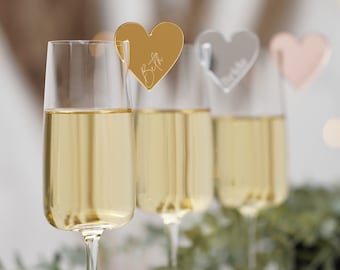 Op de afbeelding: Drie champagneflutes met gouden, zilveren en roségouden hartvormige plaatskaarten. Elke kaart heeft een naam.