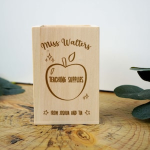 Könnte beinhalten: Ein Bleistifthalter aus Holz mit einer personalisierten Nachricht, die lautet "Miss Walters Teaching Supplies From Joshua and Tia". Der Halter zeigt einen stilisierten Apfel mit Stiel und Blatt sowie Sterne.