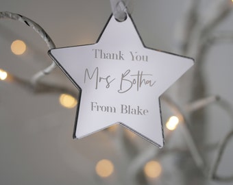 May include: A white star-shaped ornament with the text "Thank You Mrs. Botha From Blake" engraved on it.