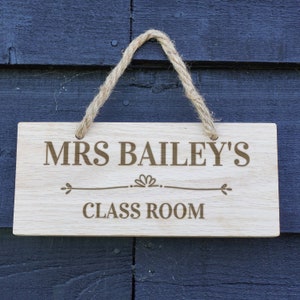 May include: A wooden sign with the text "Mrs. Bailey's Class Room" engraved on it. The sign is hanging from a rope.