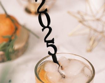 May include: A black plastic 2025 stir stick in a glass with ice and orange juice.