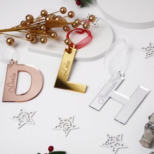 Peut inclure: Trois décorations de Noël personnalisées en acrylique. Les décorations sont en forme des lettres D, L et H. Les lettres sont en or rose, or et argent. Les noms "Darla", "Lola" et "Harrison" sont gravés sur les décorations.