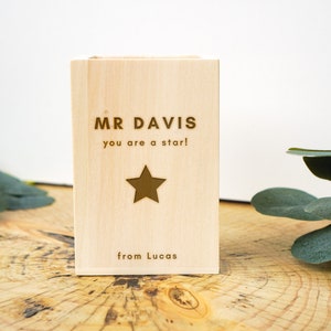 May include: A wooden box with the text "MR DAVIS you are a star! from Lucas" engraved on it. The box is light brown and has a gold star in the center.