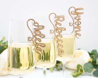 May include: Three champagne flutes with wooden name tags. The names on the tags are "Yvonne", "Rebecca", and "Helene".