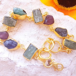 Peut inclure: Un bracelet doré orné de pierres précieuses de différentes formes et couleurs : vert, violet et bleu. Les pierres sont serties dans des montures dorées et reliées par une chaîne et un fermoir dorés.