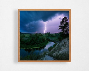 May include: A framed photograph of a lightning strike over a river and trees. The sky is dark blue with purple clouds. The river is calm and reflective.