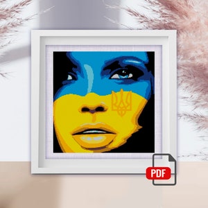 May include: A close-up of a woman's face painted in the colors of the Ukrainian flag, with the Ukrainian trident symbol on her forehead.