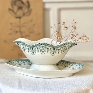 Peut inclure: Un saucier en céramique blanche avec une soucoupe ovale assortie. Le bateau et l'assiette sont décorés d'un motif floral vert sur le bord. Le saucier a un bord festonné et est rempli de fleurs séchées.