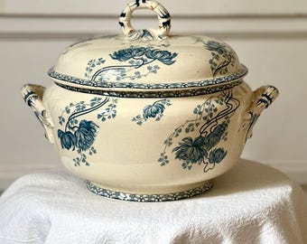 Op de afbeelding: Crèmekleurige keramische serveerschaal met deksel, versierd met blauwe bloempatronen. De schaal heeft een ronde vorm, twee zijhandvatten en een lusvormige handgreep op het deksel. De rand en de basis hebben een gestippelde rand.