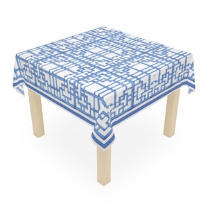 May include: A white tablecloth with a blue geometric pattern. The tablecloth is draped over a wooden table with four legs.