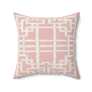 May include: A square decorative pillow with a pink background and a white bamboo-style geometric pattern. The pillow has a soft, inviting appearance, suitable for adding a touch of elegance to any living space.