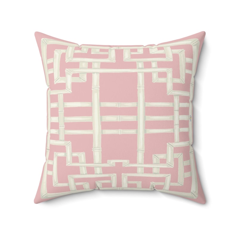 May include: A square decorative pillow with a pink background and a white bamboo-style geometric pattern. The pillow has a soft, inviting appearance, suitable for adding a touch of elegance to any living space.