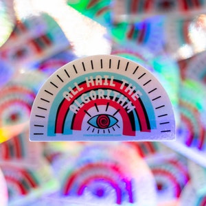 May include: A white sticker with a rainbow design and the text "All Hail The Algorithm" in black and red lettering. A stylized eye with a spiral inside is in the centre of the rainbow. The text "rosewatercreative.com" is at the bottom of the sticker.