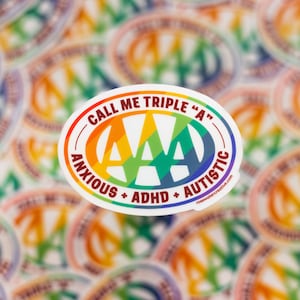 May include: A white oval sticker with a rainbow-colored "AAA" logo in the center. The text "Call me triple "A" - Anxious + ADHD + Autistic" surrounds the logo. The sticker is on a background of many other similar stickers.