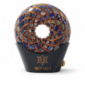 Può includere: Una sfera decorativa composta da pietre blu e grigie, racchiusa in filo di rame, poggia su una base nera. La base presenta testo dorato e un simbolo, con la scritta "NKEY FRQ 7".