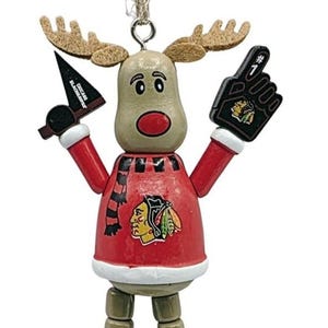 Peut inclure: Ornement décoratif de renne des Blackhawks de Chicago. Le renne porte un pull rouge avec le logo des Blackhawks, une écharpe noire et blanche, et tient un doigt en mousse et un sifflet de hockey. La base indique "Chicago Blackhawks".