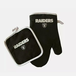 Könnte beinhalten: Schwarzes Ofenhandschuh- und Topflappen-Set mit weißer Umrandung. Das Wort "RAIDERS" ist in Silber auf beiden Artikeln zusammen mit dem Teamlogo aufgedruckt. Der Ofenhandschuh hat eine Schlaufe zum Aufhängen.