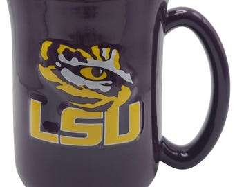 May include: A purple ceramic mug with a yellow interior and handle. The mug features the LSU logo, including a tiger eye and the letters "LSU" in yellow.