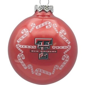 Puede incluir: Adorno navideño rojo con el logotipo de los Texas Tech Red Raiders y diseños de bastones de caramelo. El adorno tiene una tapa de metal plateado y un lazo para colgar. El texto "TEXAS TECH RED RAIDERS" es visible.