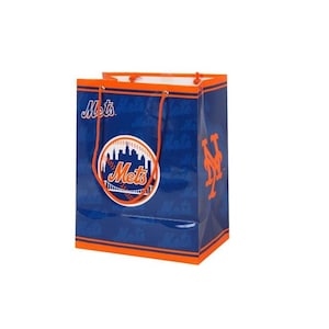 May include: A blue gift bag with orange accents and handles. The bag features the New York Mets logo, a baseball with a cityscape, and the team's name. The bag is a rectangular shape.