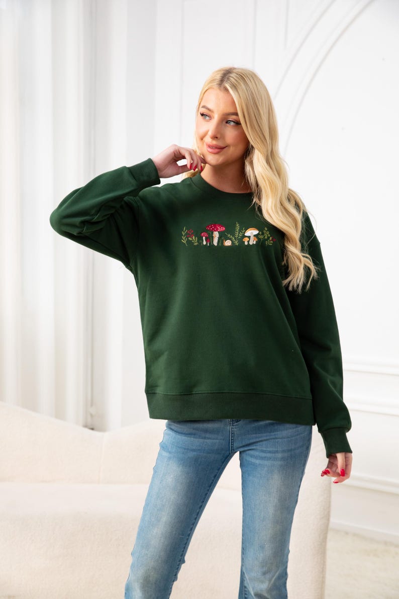 Op de afbeelding: Een donkergroen sweatshirt met een geborduurd ontwerp van paddenstoelen en bladeren. Het sweatshirt heeft een ontspannen pasvorm en een ronde hals.