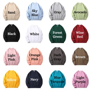 Op de afbeelding: Een set van 16 crewneck sweatshirts in verschillende kleuren, waaronder zand, hemelsblauw, grijs, avocado, zwart, wit, bosgroen, wijnrood, lichtroze, oranje roze, donkergrijs, bruin, geel, marine, blauw turquoise en lichtpaars. Elk sweatshirt heeft een andere kleur en een tekstlabel met de kleurnaam.