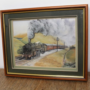 May include: Framed watercolor painting of a steam train traveling through a valley. The train is emitting smoke and is surrounded by green hills and a cloudy sky.