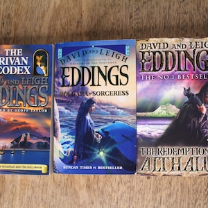 May include: Three fantasy paperback books by David and Leigh Eddings. The first book is titled "The Rivan Codex" and features a white owl and a wolf on the cover. The second book is titled "Polgara - Sorceress" and features a woman in a blue dress standing on a rocky shore. The third book is titled "The Redemption of Althalus" and features a person in a black cloak holding a black cat.