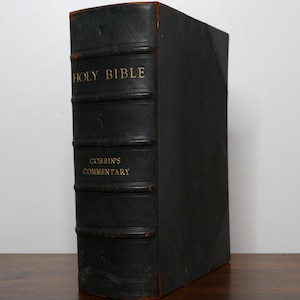 May include: A vintage, black leather-bound book titled "Holy Bible" and "Cobbin's Commentary" in gold lettering. The book has a worn appearance, suggesting age and use. The spine features horizontal bands.