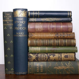 Könnte beinhalten: Ein Stapel antiker Bücher mit verschiedenen Farben und Designs. Titel sind u.a. "The Story of Greece" und "Adam Bede". Die Bücher haben goldene Schrift und dekorative Elemente, was auf eine Vintage-Sammlung hindeutet.