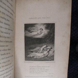 May include: An open book with the title "PARADISE AND THE PERI" above a black and white illustration. The illustration depicts a winged figure and two figures lying down. Text is visible on the page.