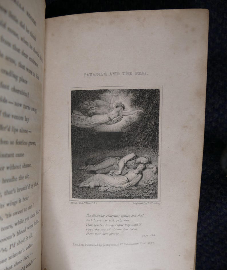 May include: An open book with the title "PARADISE AND THE PERI" above a black and white illustration. The illustration depicts a winged figure and two figures lying down. Text is visible on the page.