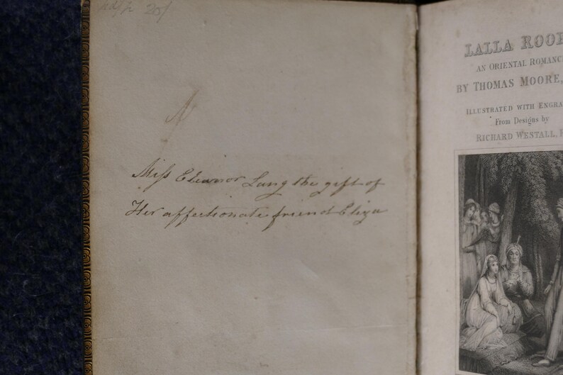 May include: Open book with handwritten inscription: "Miss Eleanor Lung the gift of His affectionate friend Eliza." The right page displays the title "Lalla Rookh" by Thomas Moore, with illustrations.