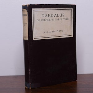 Peut inclure: Un livre à couverture rigide intitulé "Daedalus or Science and the Future" de J.B.S. Haldane. Le livre a une couverture sombre avec une étiquette rectangulaire portant le titre et le nom de l'auteur. La tranche est de couleur plus claire avec le titre "Daedalus".