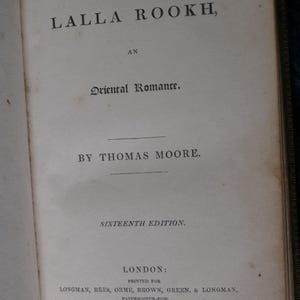 May include: Open book page with the title "LALLA ROOKH, AN Oriental Romance" by Thomas Moore. The text is in black ink on aged, off-white paper. The book is a sixteenth edition, printed in London in 1832.