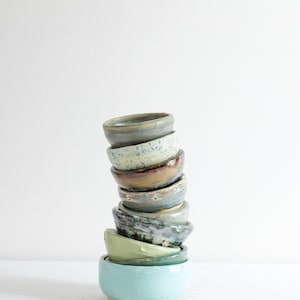 May include: A white ceramic mug with a black handle and the text "But First, Coffee" in a black, handwritten-style font. The mug is on a white surface.