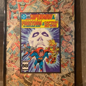May include: A framed comic book cover featuring Superman, Firestorm, and Captain Atom. The cover is a collage of various comic book covers, with a blue, purple, and yellow color scheme. The text on the cover reads "DC Comics Presents Superman & Firestorm & Captain Atom. The Nuclear Man."