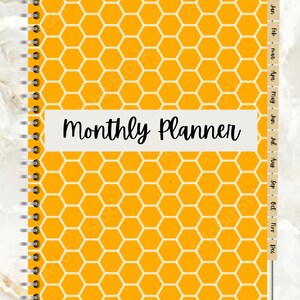 May include: A yellow monthly planner with a honeycomb pattern and a white tab for each month of the year. The text "Monthly Planner" is printed in black on a white banner.