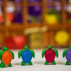 May include: Four small plastic turtle figurines in a line. The turtles are green with orange, blue, red, and purple shells.