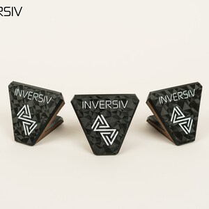 May include: Three black triangular stands with a geometric pattern and the word "INVERSIV" printed in white. The stands are made of a textured material and have a wooden base.